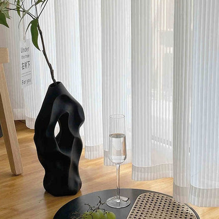 Valkoinen pystysuoraan laskostettu valkoverho