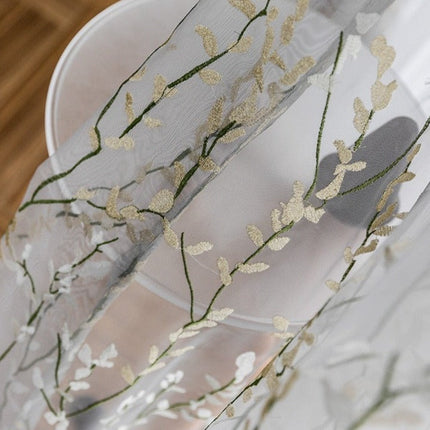 Läpikuultava verho kirjaillulla oksakuviolla