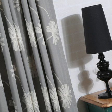 Harmaa verho brodeeratuilla päivänkakkaroilla