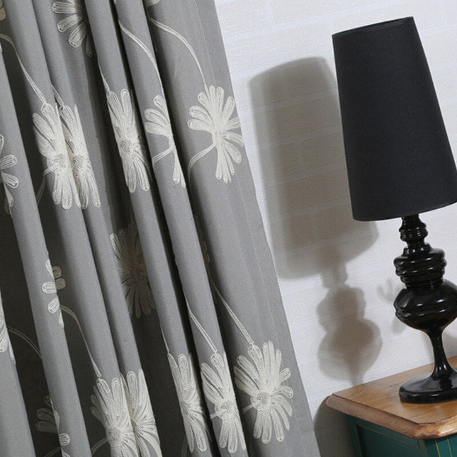 Harmaa verho brodeeratuilla päivänkakkaroilla